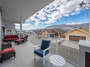 A balcony with outdoor furniture, a clear view of houses, and a mountainous landscape. - Quail Cottage with complimentary Golf Cart #187 (Osoyoos)