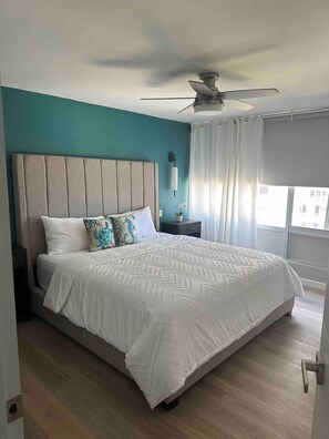 A bedroom with a large bed, a ceiling fan, a nightstand, and a window with curtains. - Spectacular Apt With Beach View (Carolina)