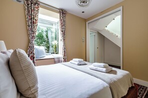 Ein Hotelzimmer mit Bett, einem fenster mit Vorhängen, Blick auf Grünfläche außerhalb und einer Tür, die zu einer oberen Ebene führt.