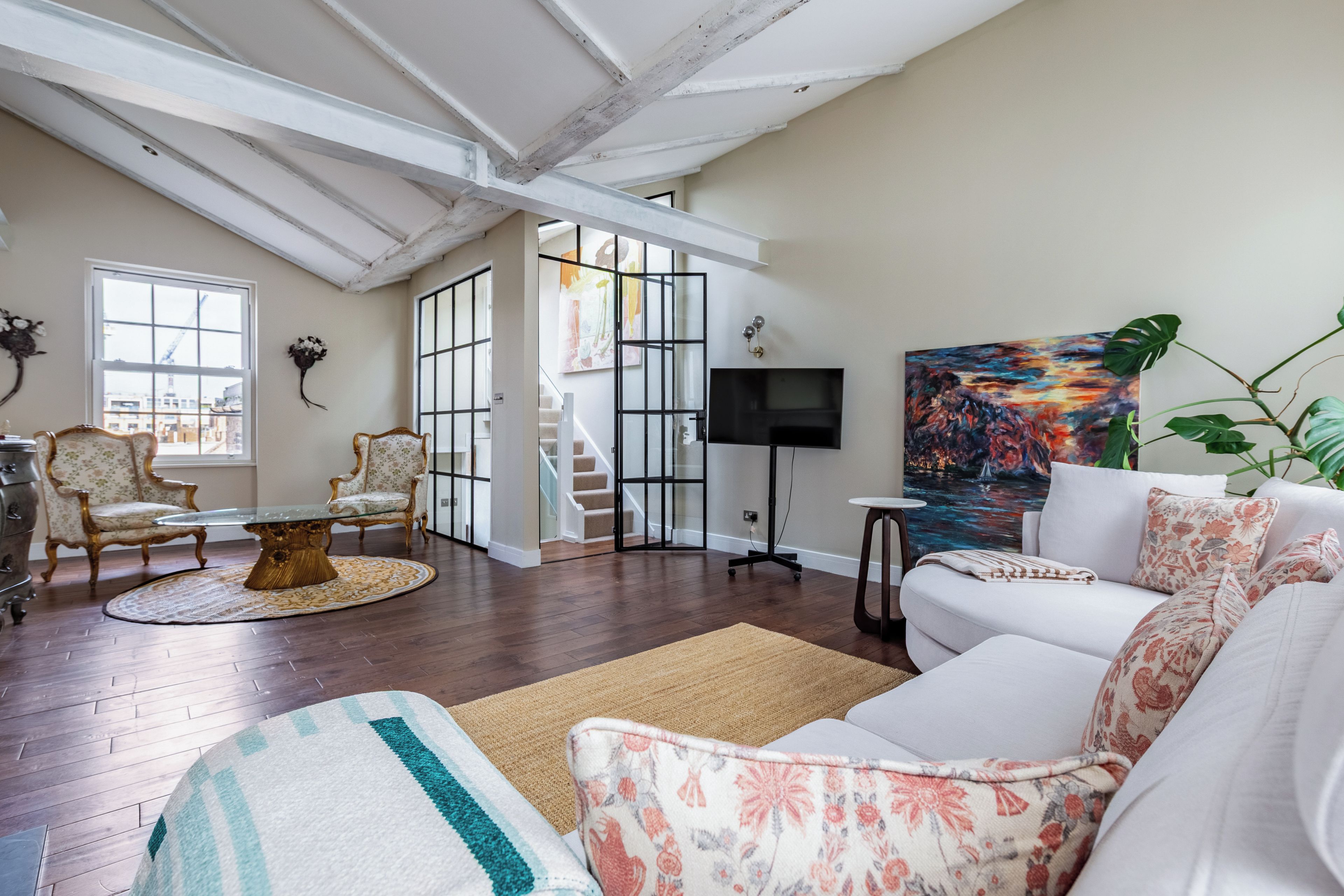 A spacious living room with a high ceiling, a fireplace, a television, and a large window.