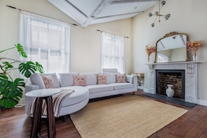 A living room with a white sofa, a round coffee table, a fireplace, and a large window. - Luxury 4-Bed House | Kensington, Notting Hill & Holland Park. (London)
