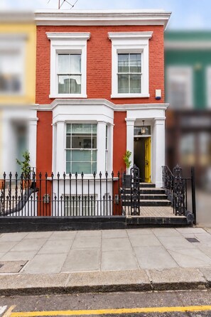 A two-story red brick house with white trim, a black iron fence, and a yellow door. - Luxury 4-Bed House | Kensington, Notting Hill & Holland Park. (London)