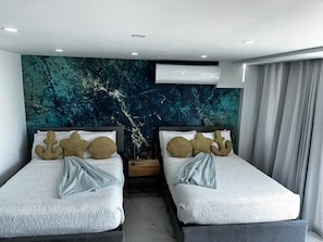 Een hotelkamer met twee bedden, een groot abstract schilderij aan de muur, een airconditioning en een raam met gordijnen.