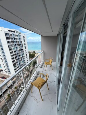 A balcony with two yellow chairs, a glass door, and a view of the ocean and buildings. - Aqua Luxury Modern Beach Apartment (Carolina)