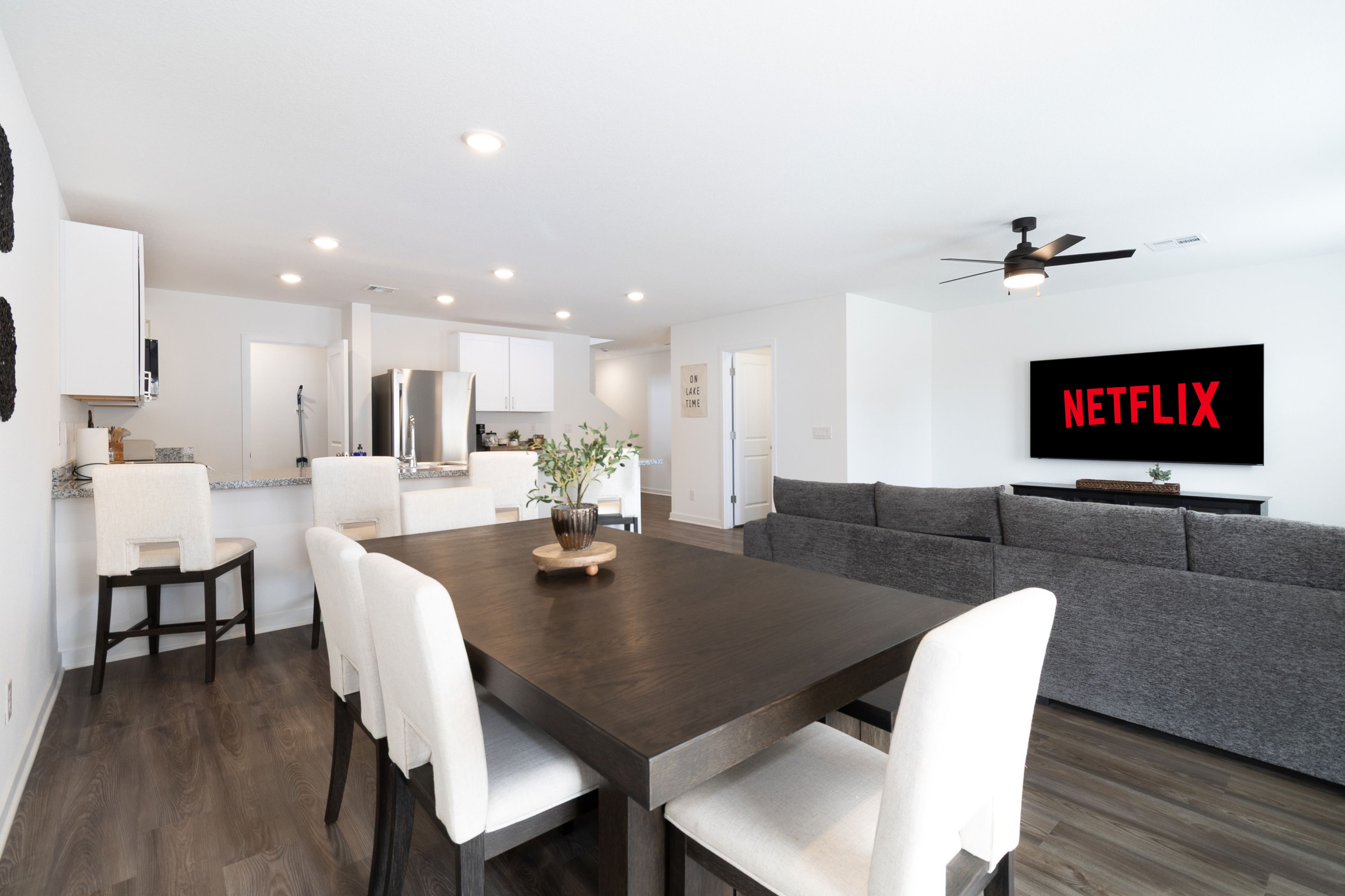 A modern living space with a dining area, kitchen, and a large flat-screen TV mounted on the wall.
