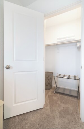 A closed white door with a silver handle, a beige carpeted floor, a beige waste basket, and a metal drying rack with a white towel hanging on it. - Luxe Townhome near Lake Mohave & Laughlin (Bullhead City)