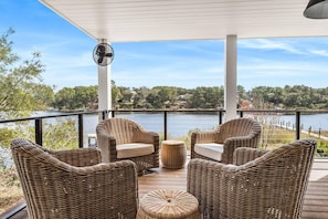A covered outdoor seating area with wicker furniture and a fan, overlooking a lake with trees and a dock. - Bella Vista (Santa Rosa Beach)