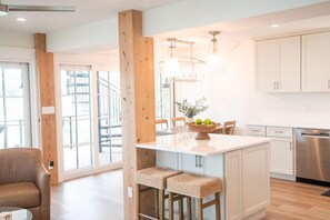 A modern kitchen with a central island, wooden beams, and a dining area with chairs. - Bella Vista (Santa Rosa Beach)