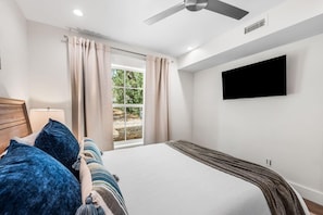 A bedroom with a bed, a TV mounted on the wall, a ceiling fan, and a window with curtains. - Bella Vista (Santa Rosa Beach)