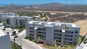 Um moderno complexo de apartamentos com vários andares, área de estacionamento e vista para a paisagem desértica com montanhas ao longe.