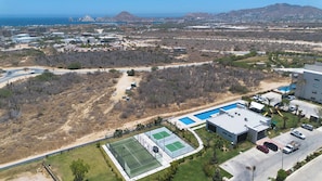 Uma área residencial com piscina, quadras de tênis e uma rua com carros.