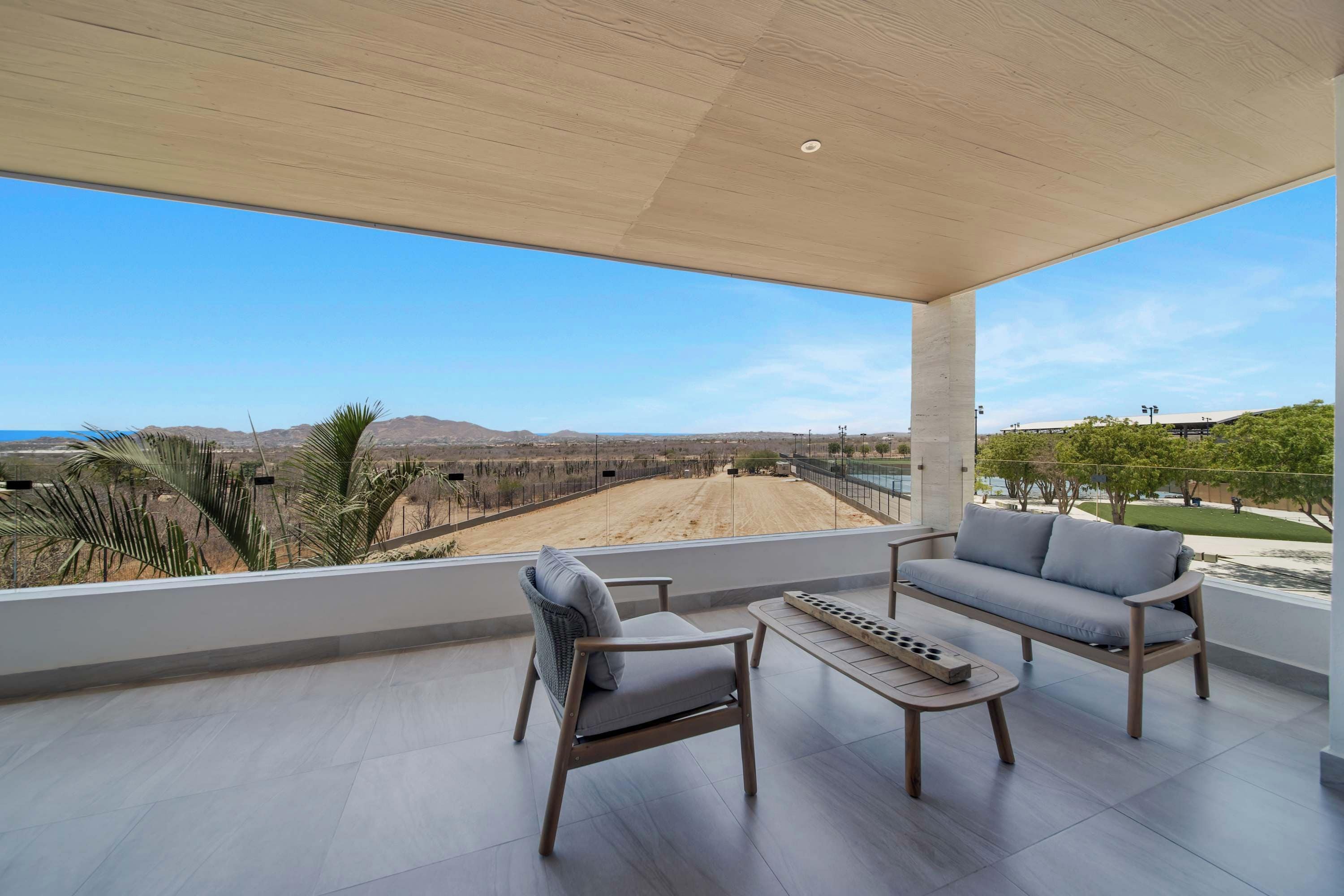 A spacious balcony with a view of a desert landscape, a sofa, a chair, and a small table.