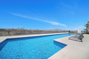 Uma piscina retangular com água azul cristalina, rodeada por um deck revestido com azulejos.