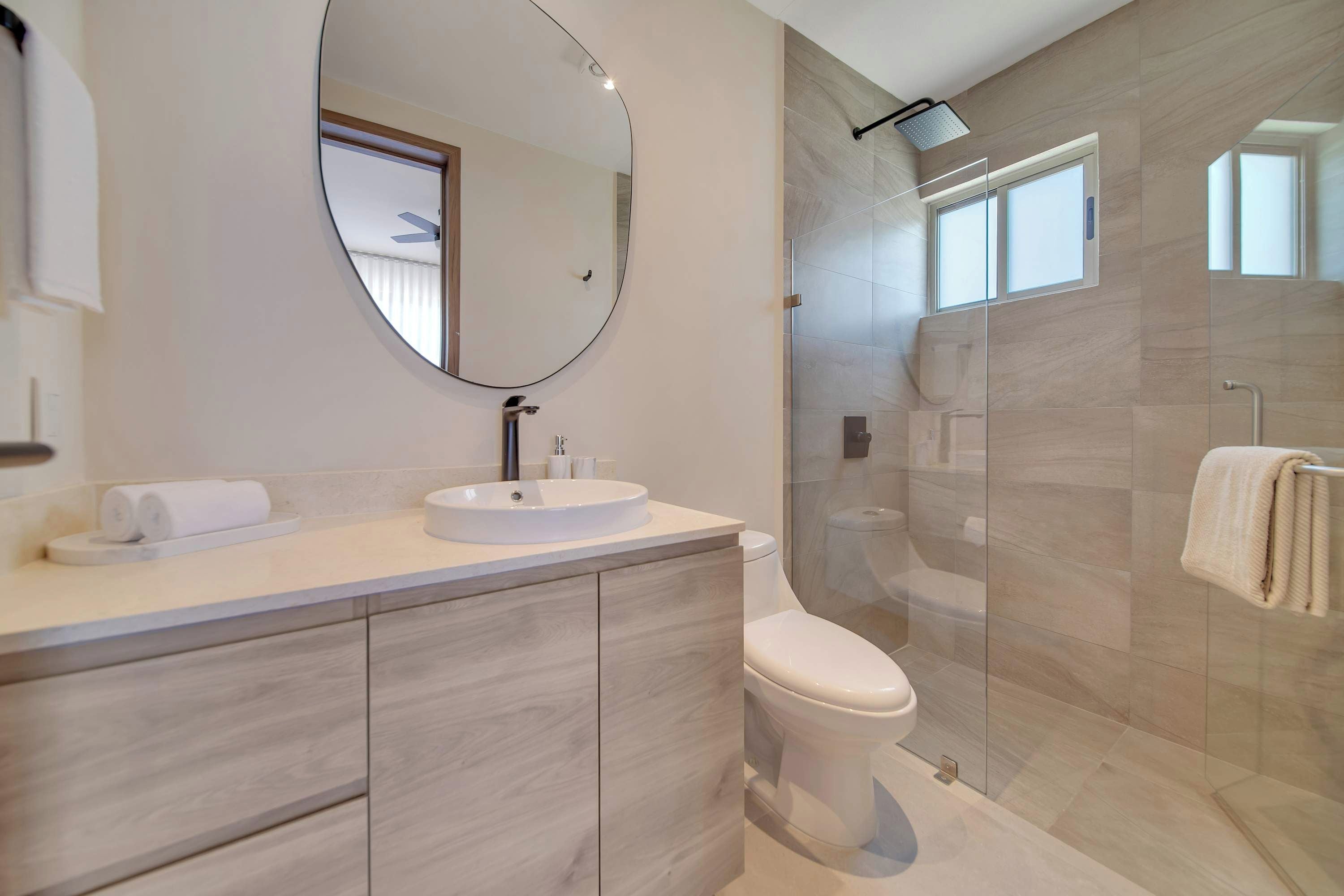 A modern bathroom with a round mirror, a sink, a toilet, and a glass-enclosed shower area.