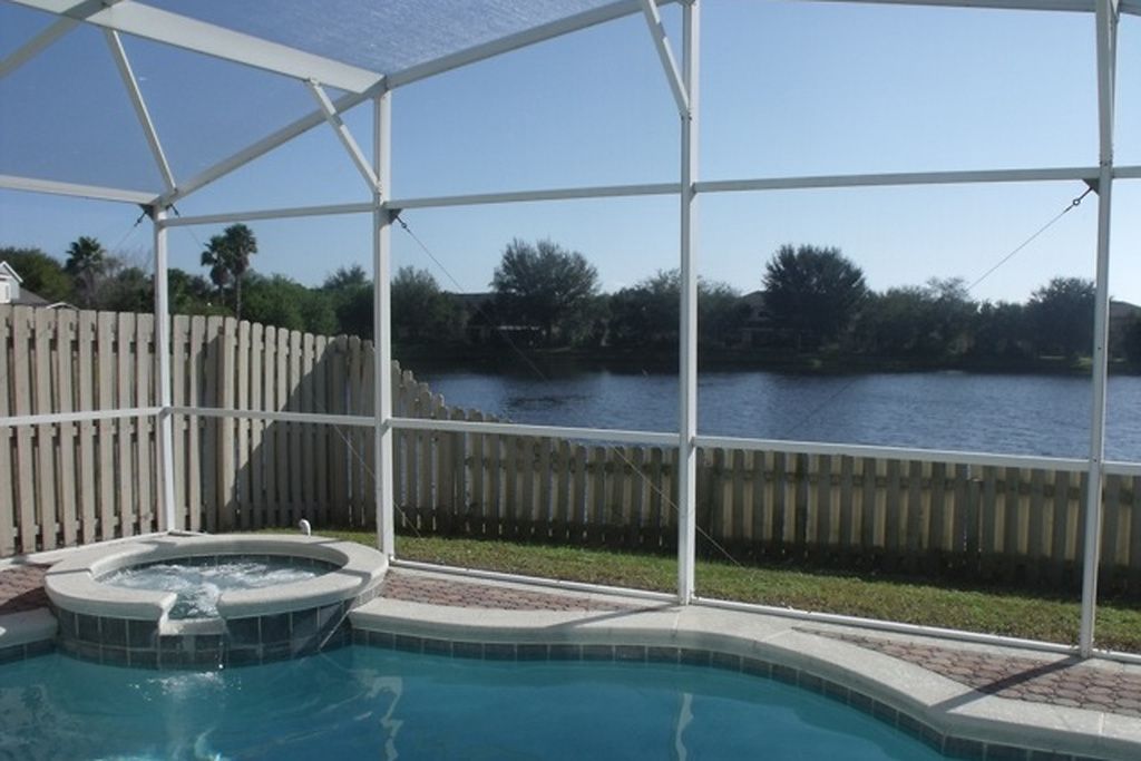 A swimming pool with a hot tub, surrounded by a wooden fence and a view of a body of water.