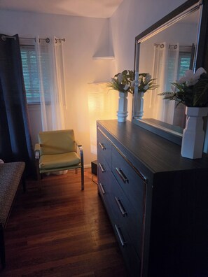 Ein Zimmer mit Holzboden, einem gelben Sessel, einem Schminktisch mit Spiegel und einer Lampe.