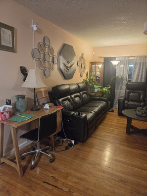 A living room with a leather sofa, a wooden desk with a computer, a lamp, and decorative wall art. - Awesome 3-bedroom house with AC in Fort Washington near National Harbor & MGM (Fort Washington)