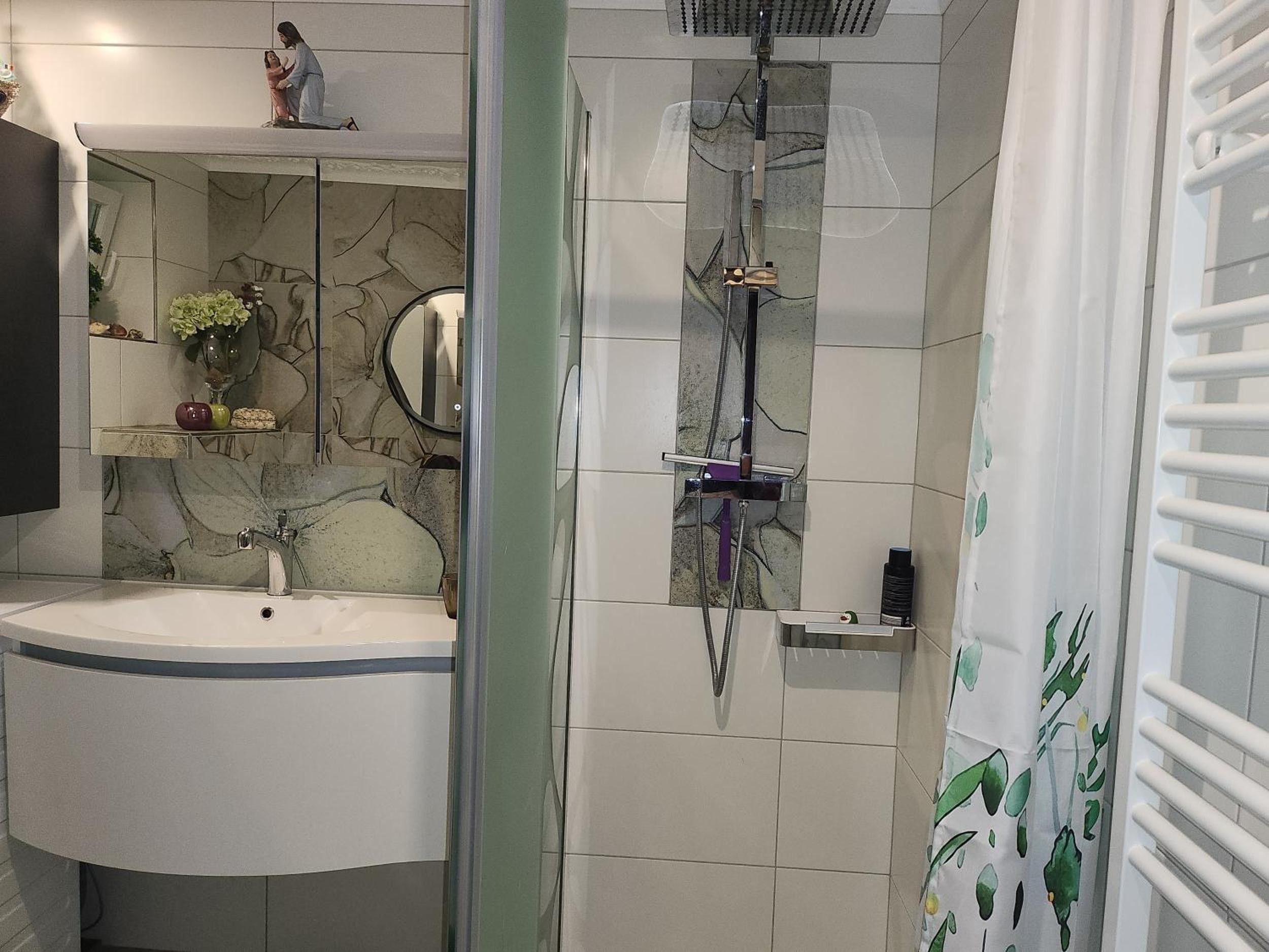 A bathroom with a sink, mirror, shower, and a towel rack.