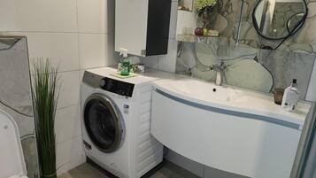 A modern bathroom with a built-in washing machine, a sink, and a mirror.