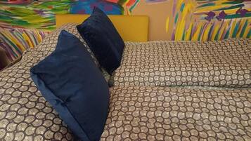 A bed with patterned bedding and two pillows, set against a colorful abstract wall art.