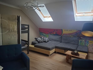 A loft-style room with a bunk bed, a sofa, a small table, and a colorful mural on the wall. - Apartment 'Naturparadies' with Mountain View, Balcony and Wi-Fi (Marktl)