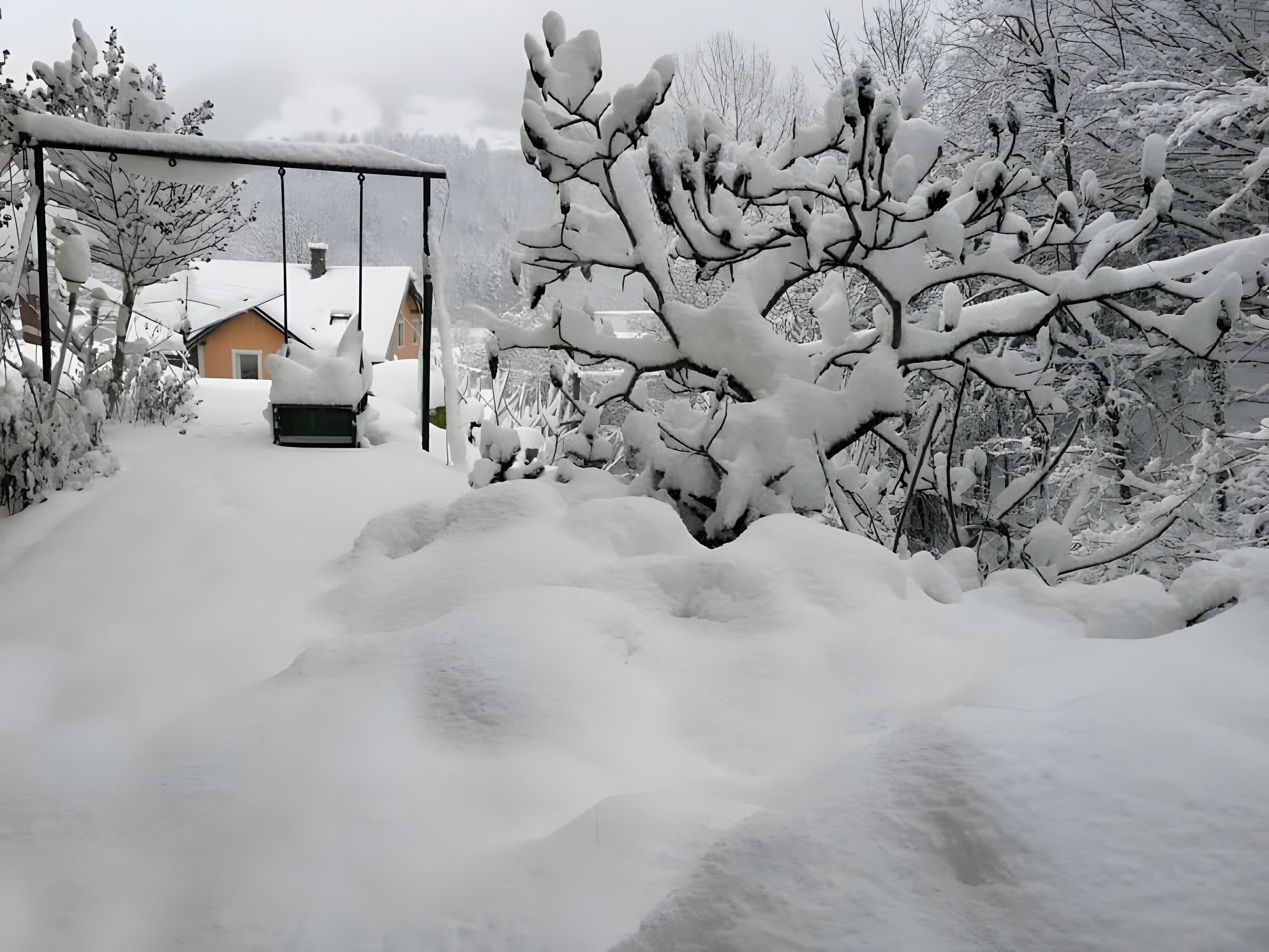 Caminho coberto de neve que leva a uma casa com garagem e portão de metal.
