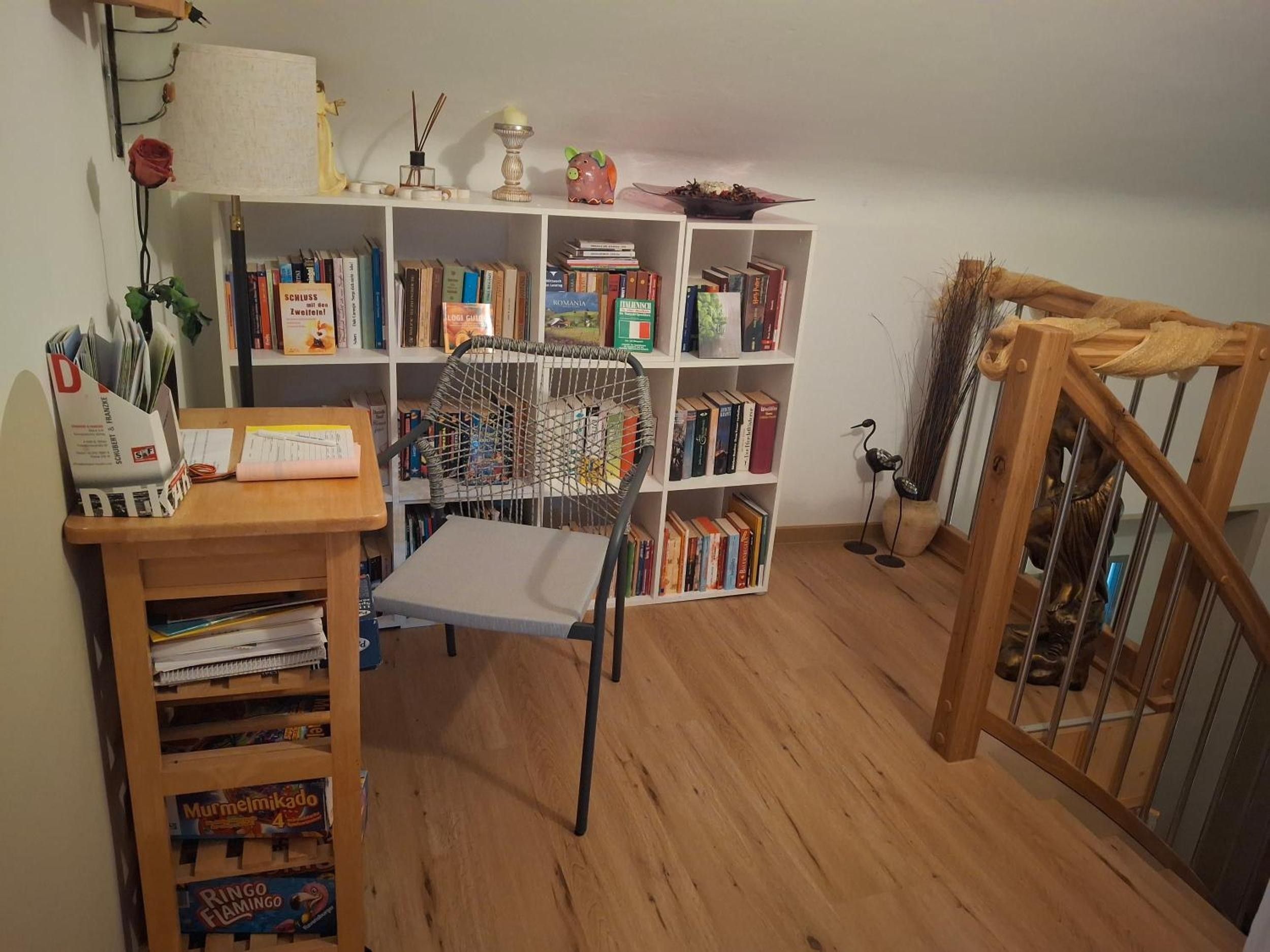 A room with a bookshelf, a chair, a wooden desk, and a small statue.