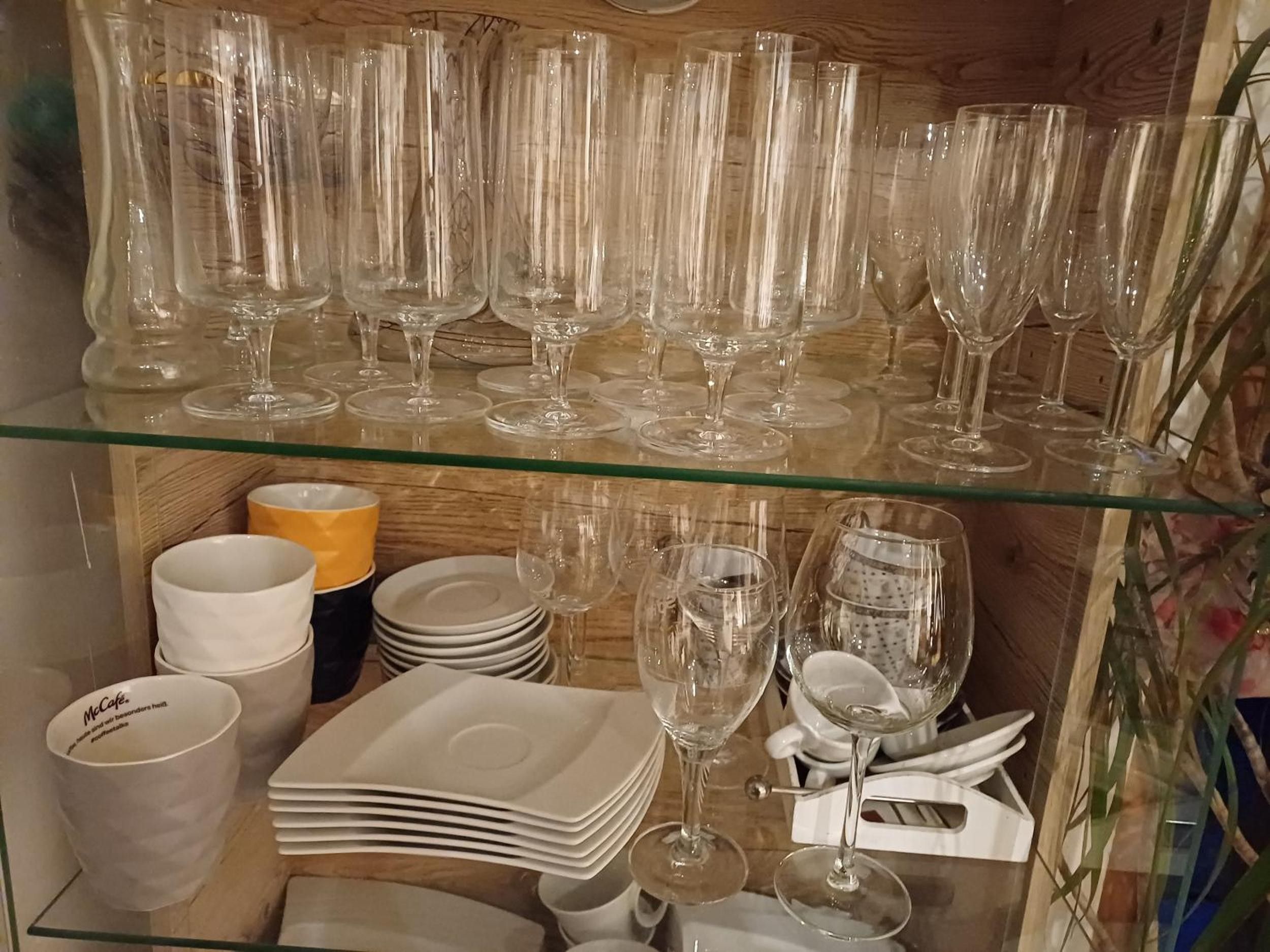 Una estantería de vidrio exhibe copas de vino, vasos y platos.