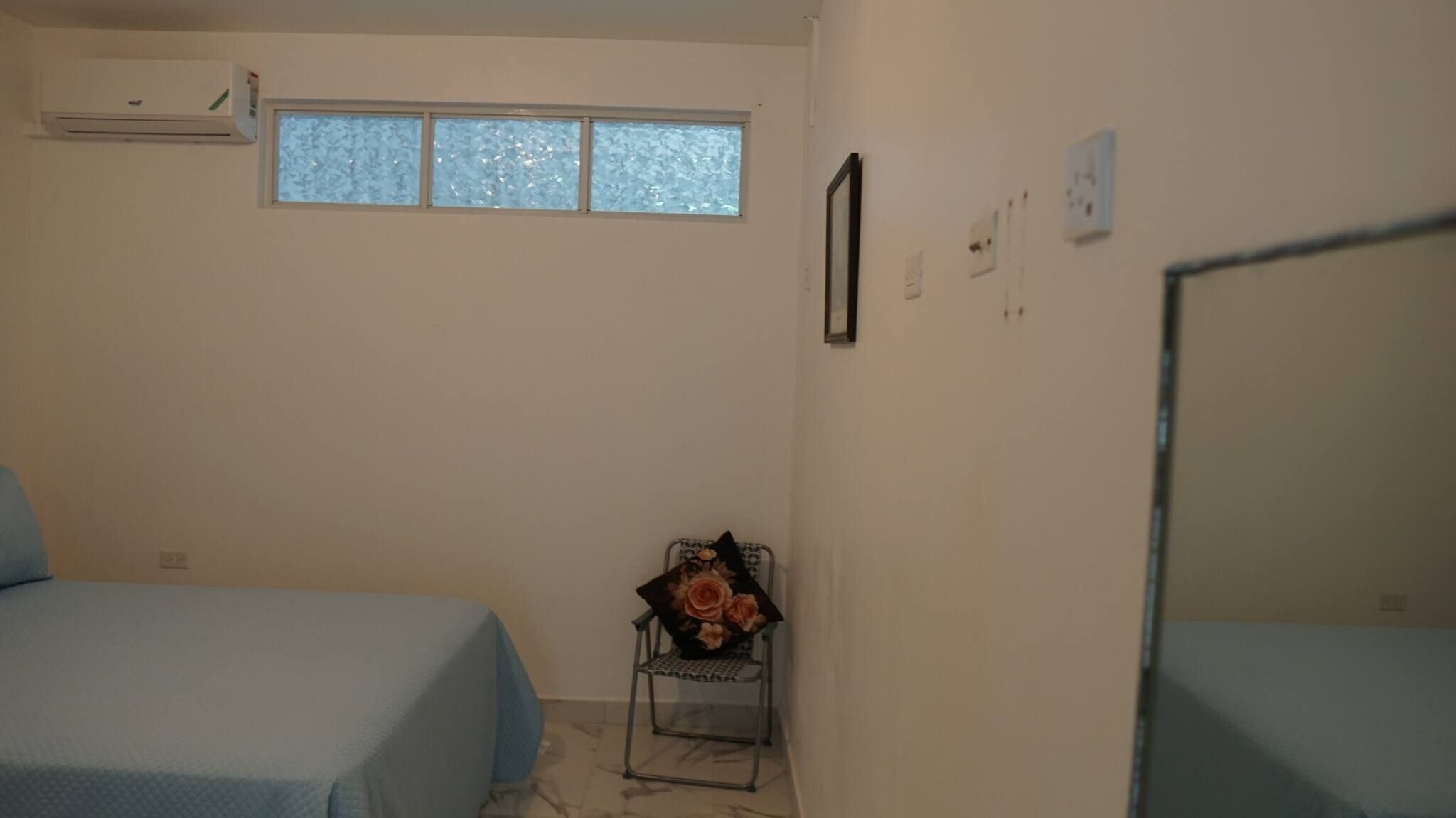 Een kamer met twee bedden, een klein raam en een stoel met een bloemstuk.