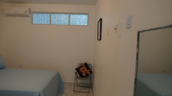 A room with two beds, a small window, and a chair with a floral arrangement.