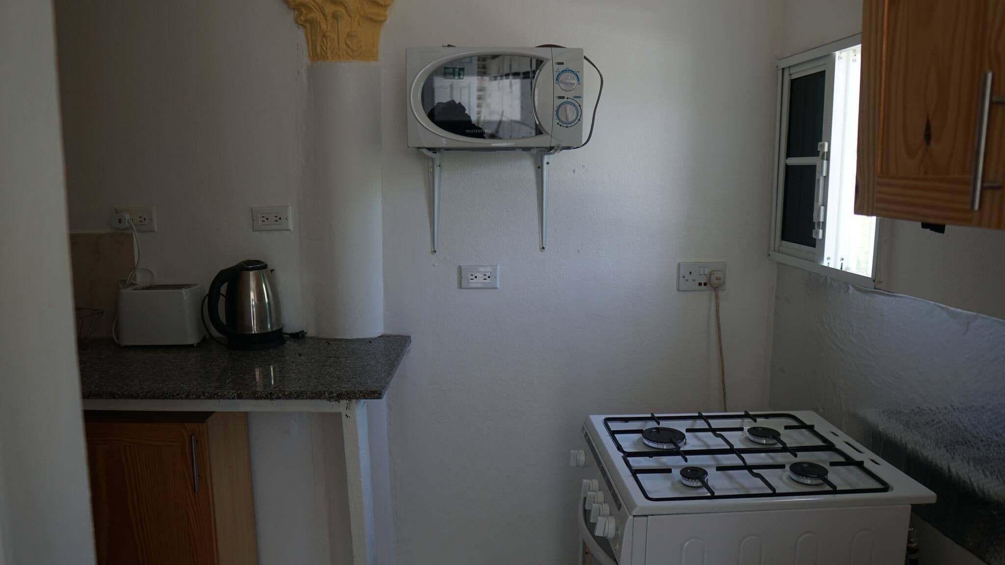 Uma cozinha compacta com micro-ondas, fogão a gás, torradeira e chaleira.
