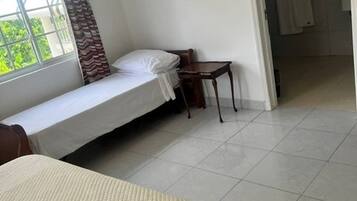 Quarto com uma cama de solteiro, uma mesinha e uma janela com cortinas.