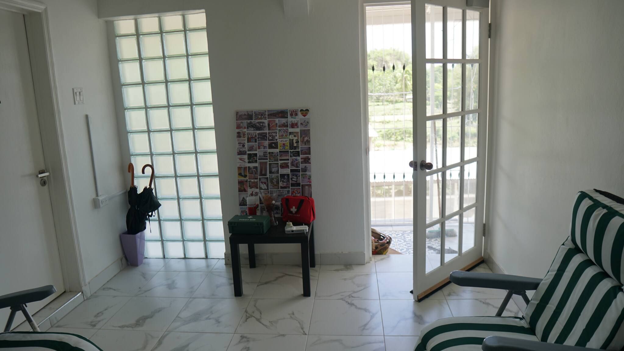 Une pièce avec un sol carrelé, un banc, une table sur laquelle se trouve un sac rouge, et un mur orné d’un collage de photos.