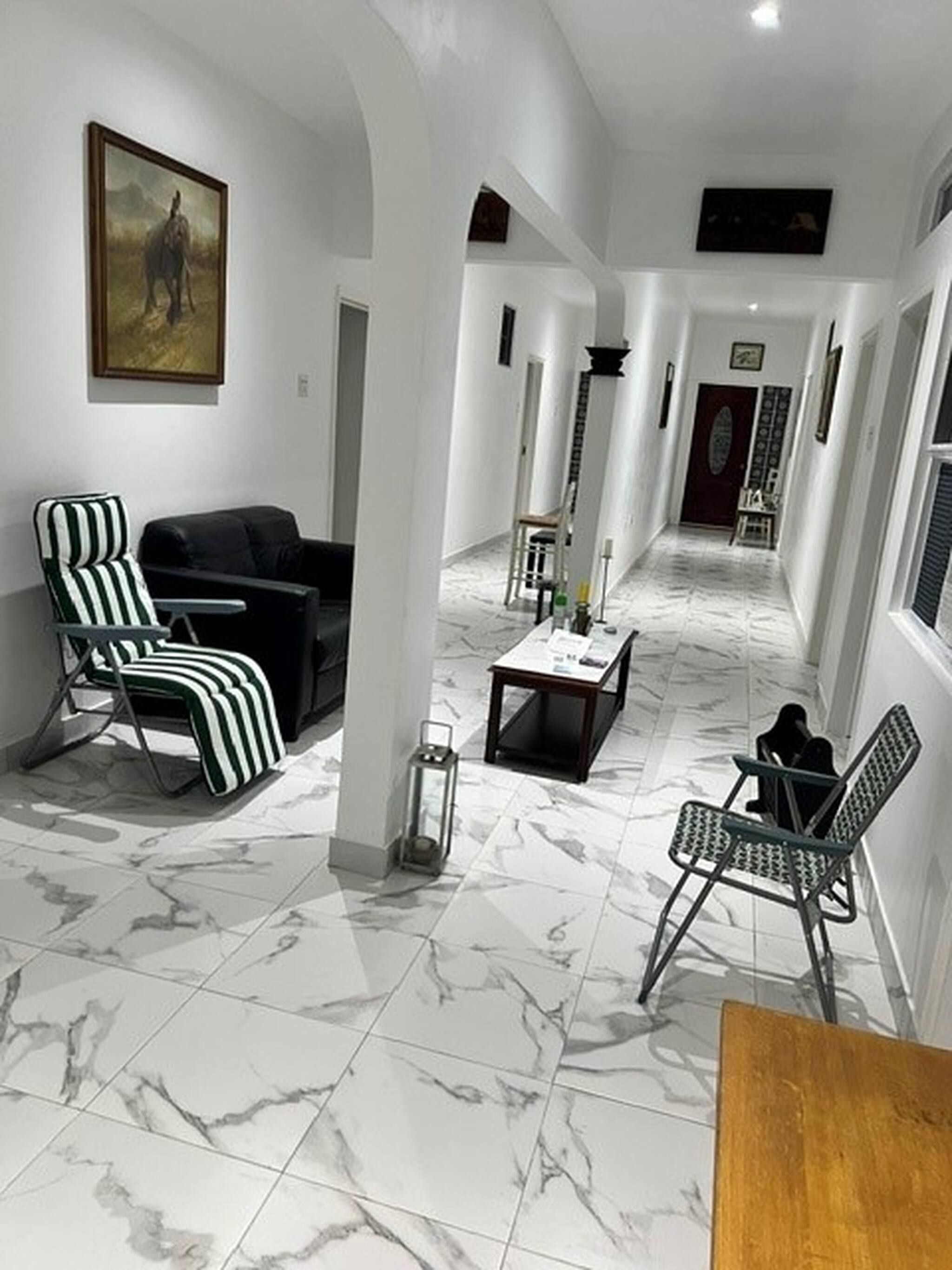 Un hall spacieux doté d’un sol en marbre, d’un canapé en cuir noir, d’un fauteuil à rayures et d’une petite table sur laquelle est posée une bougie.