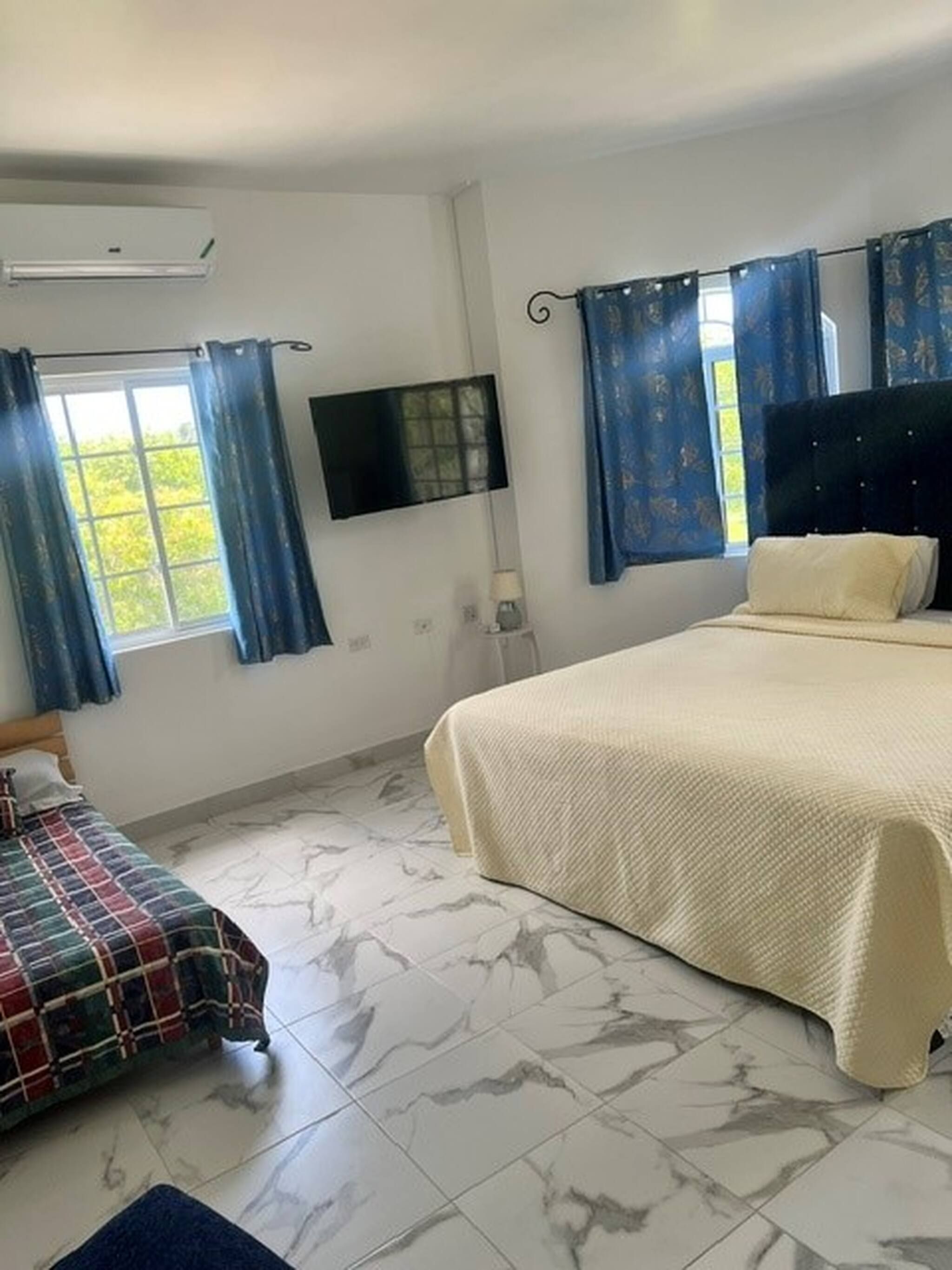 A bedroom with a bed, a TV, a window with curtains, and a small table.