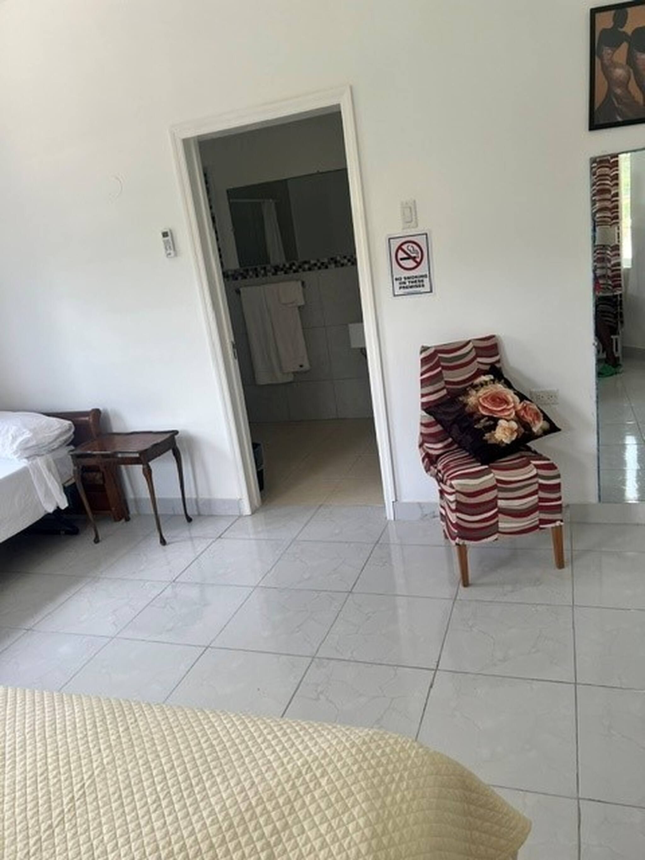 A hotel room with a bed, a chair, a small table, a bathroom visible through an open door, and a no-smoking sign on the wall.