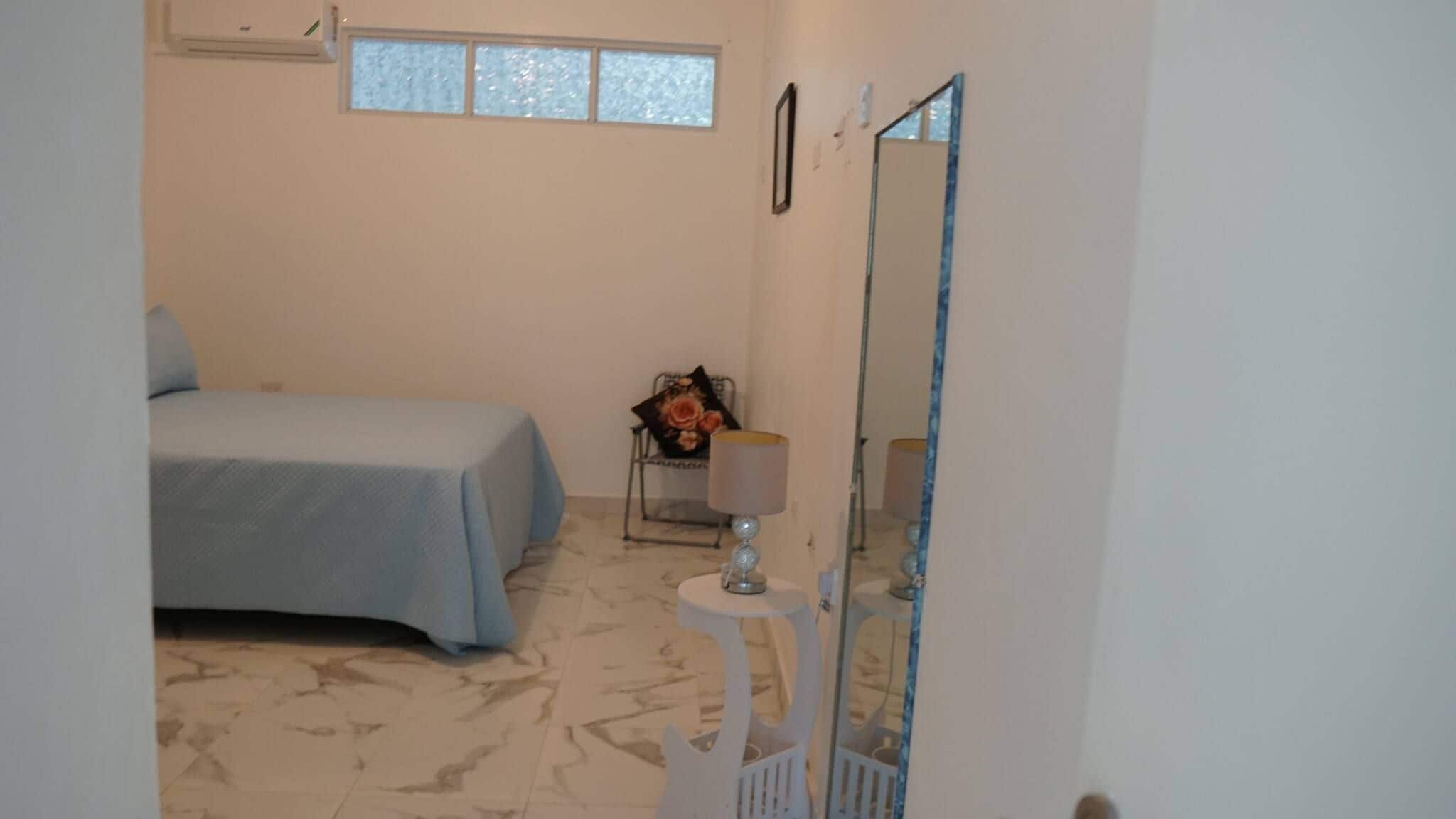 Ein Schlafzimmer mit einem Bett, einem Sessel, einem Tisch mit Lampe und einem Spiegel.