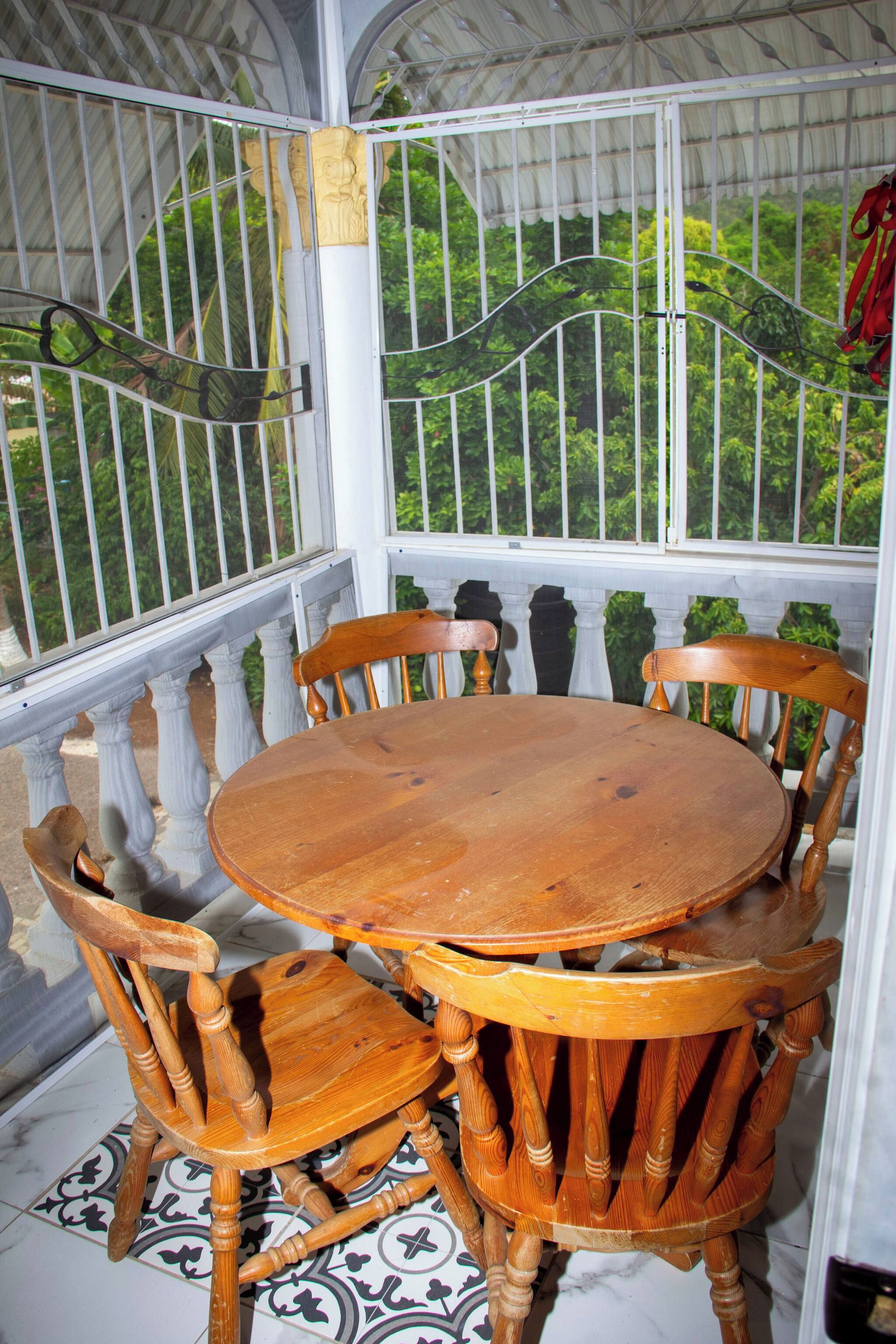 Een overdekt terras met een ronde houten tafel en zes stoelen.