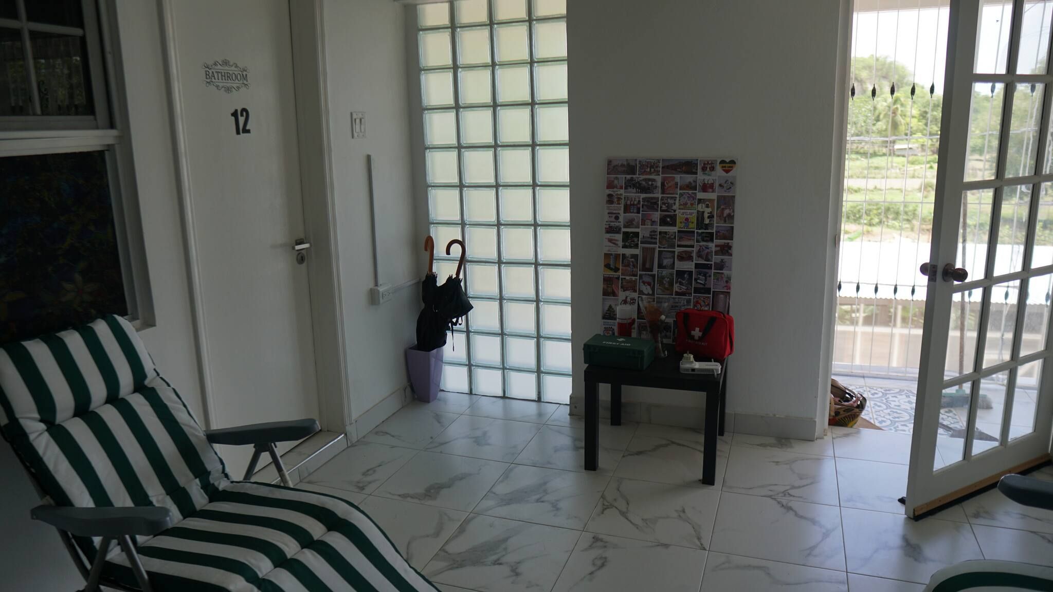Quarto com uma cadeira listrada, uma mesa pequena com uma bolsa vermelha e uma parede de fotografias.