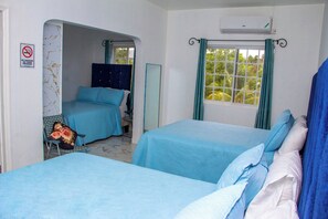 A hotel room with two beds, a sitting area with a chair and a table, a window with curtains, and a no-smoking sign on the wall.