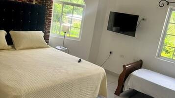 Een slaapkamer met een bed, een nachtkastje, een aan de muur bevestigde televisie en een raam met gordijnen.