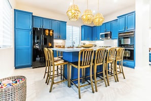 A modern kitchen with blue cabinets, a central island, and a black refrigerator. - Villa Ja'Dore Long Term! (Cathedral City)