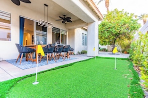 A patio with a dining table and chairs, a ceiling fan, and a small lawn with two flags. - Villa Ja'Dore Long Term! (Cathedral City)