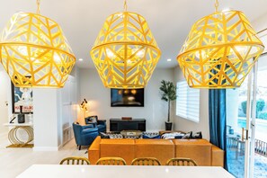 A dining area with a long table and chairs, a blue sofa, and a decorative lamp. - Villa Ja'Dore Long Term! (Cathedral City)