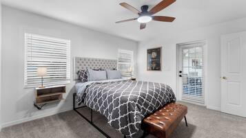 A bedroom with a bed, a bench, a ceiling fan, and a door.