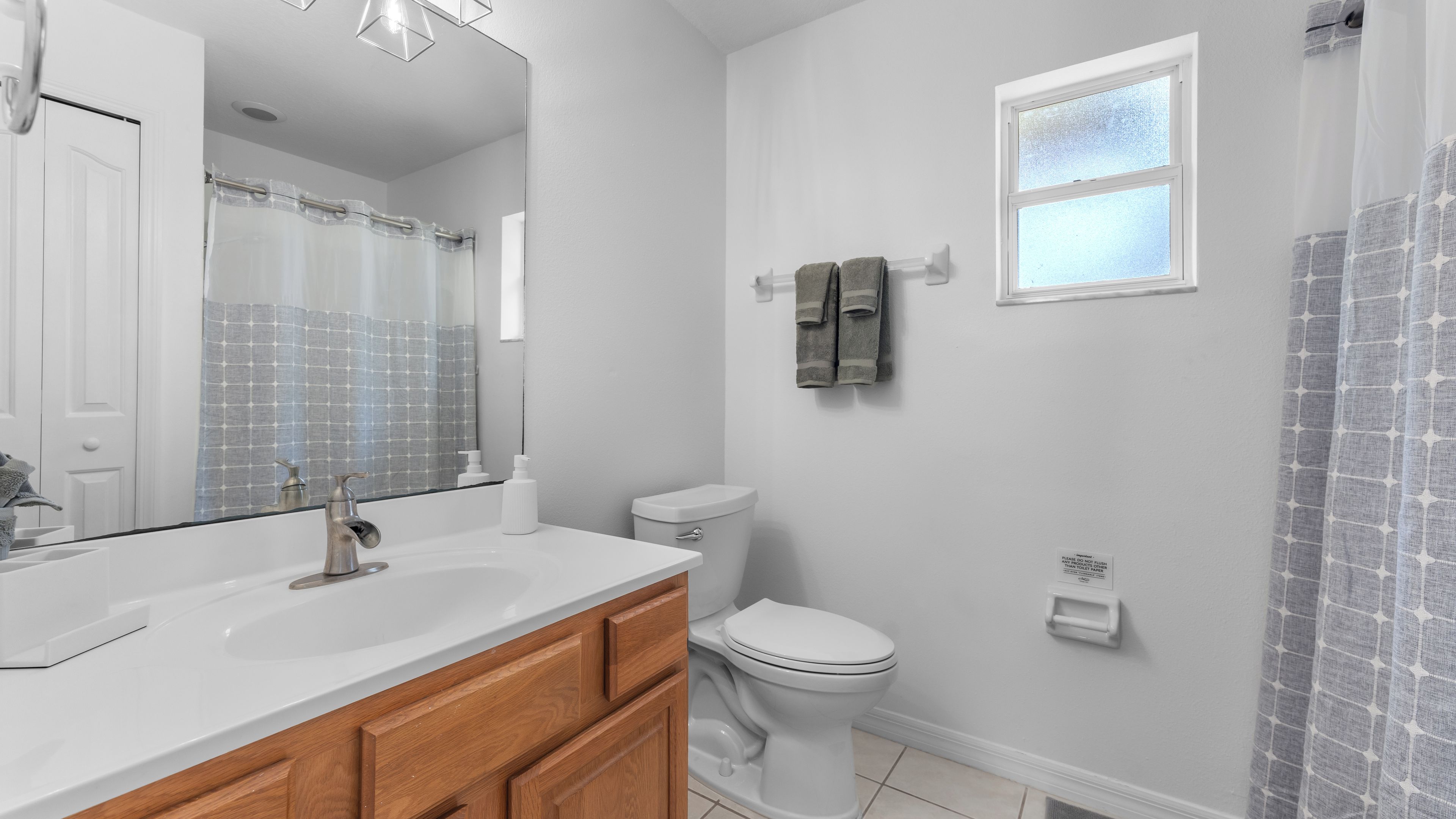 A bathroom with a white sink, wooden vanity, a toilet, a mirror, and a shower curtain.