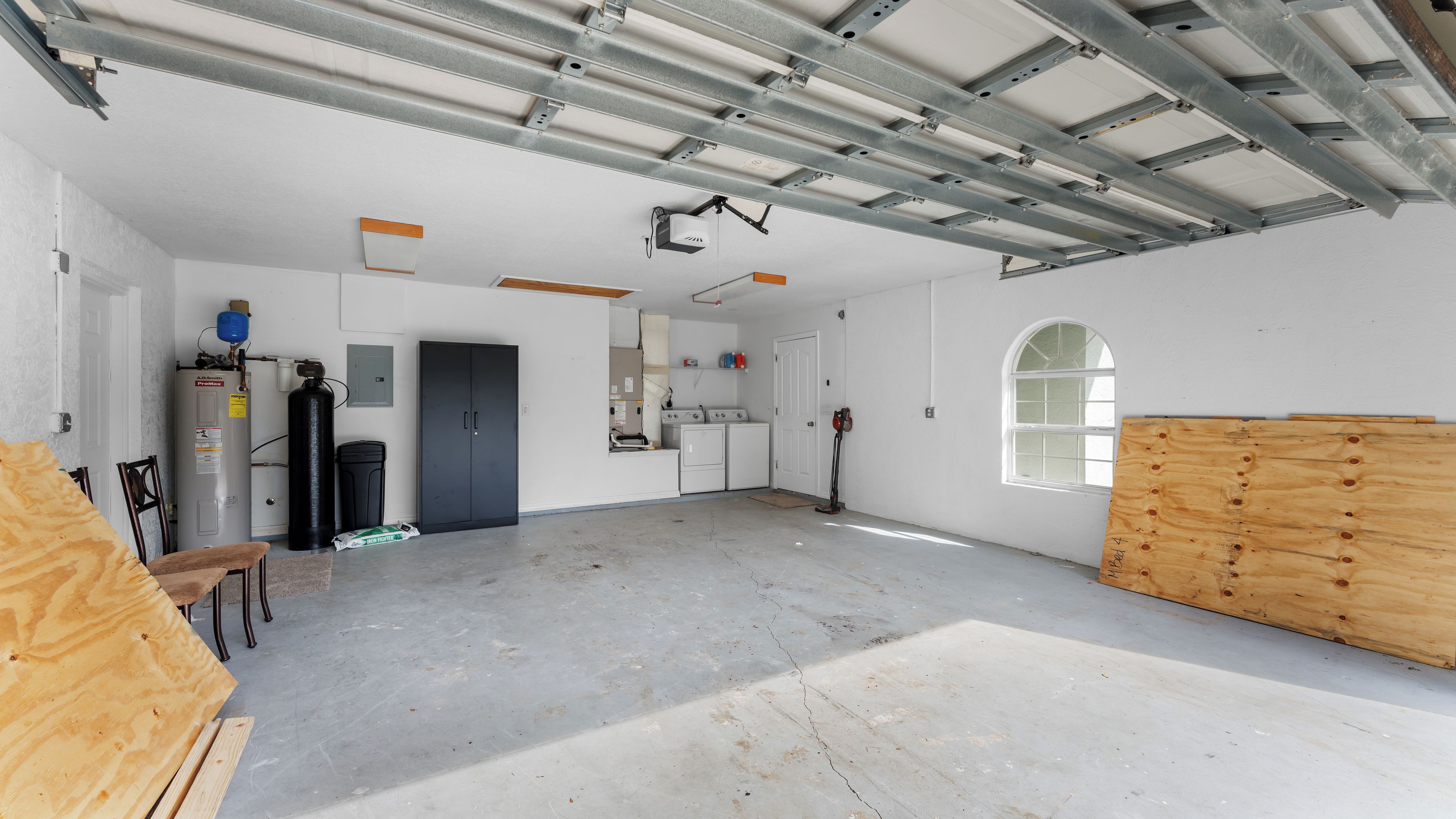 Een ruime garage met een betonnen vloer, een boiler, een wasmachine en een grote houten deur.