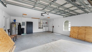 Eine geräumige Garage mit Betonboden, Warmwasserbereiter, Waschmaschine und einer großen Holztür.