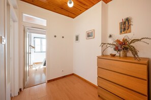 A room with wooden flooring, a wooden dresser, a door leading to another room, and a ceiling with wooden beams. - GuestReady-Charming Lisbon Retreat (Lisbon)