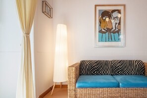 A room with a wicker sofa, a standing floor lamp, and a framed artwork on the wall. - GuestReady-Charming Lisbon Retreat (Lisbon)